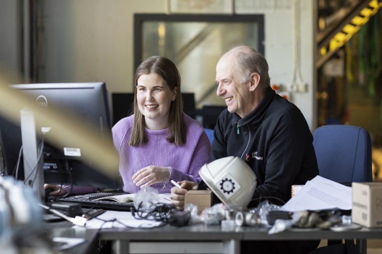 Kaksi henkilöä katsoo läppäriä työpöydän ääressä.