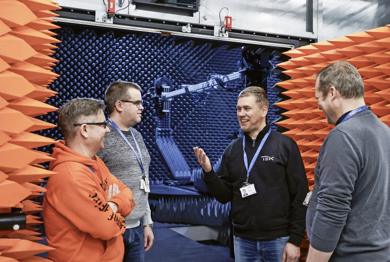 Harri Kaarre (vasemmalla), Mika Mäntymäki, Marko Honkalampi ja Marko Määttä juttelevat viikonlopun ylitöistä CATR-kammion (Compact Antenna Test Range) edessä. Oranssit piikit ovat absorbereita, jotka vaimentavat signaalit.