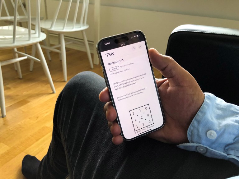 Kotioloissa istuva henkilö pitää kädessään kännykkää, jossa on auki Divisium-3-peli.