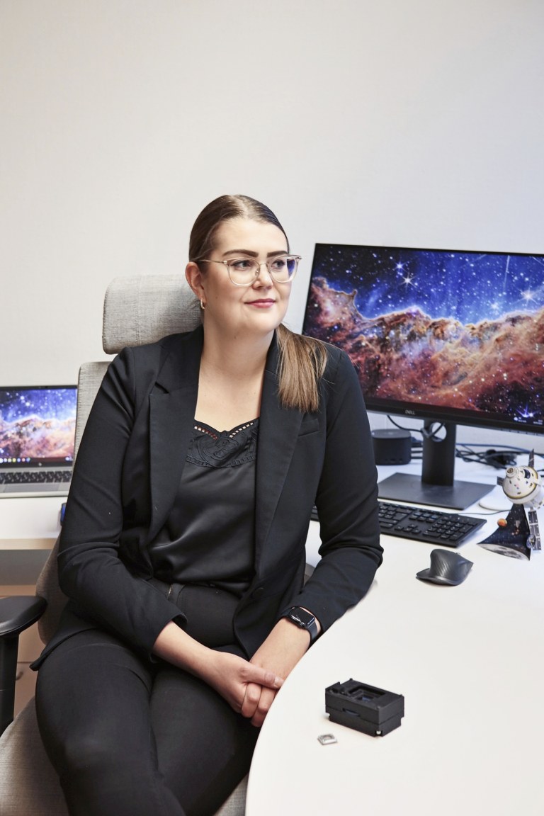 Kiira Tiensuu istuu tietokoneen edessä, tietokoneen näytöllä on avaruusmaisema.