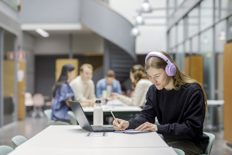 Opiskelija täyttää kalenteriaan kuulokkeet päässään.
