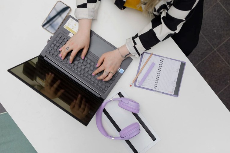 Ylhäältä päin otettu kuva henkilöstä, joka käyttää kannettavaa tietokonetta.