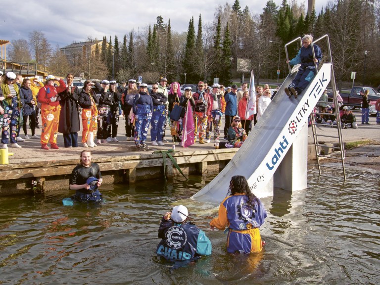 Ihmisiä kerääntyneenä katsomaan, kun opiskelijat laskevat liukumäellä veteen.