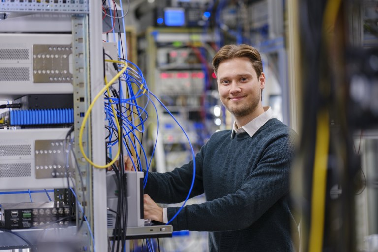 Tuomas Uusnäkki katsoo kameraan johtojen takaa.