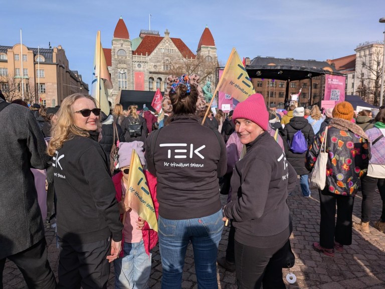 TEKin edustajat seisovat Rautatientorilla, jossa on paljon ihmisiä.