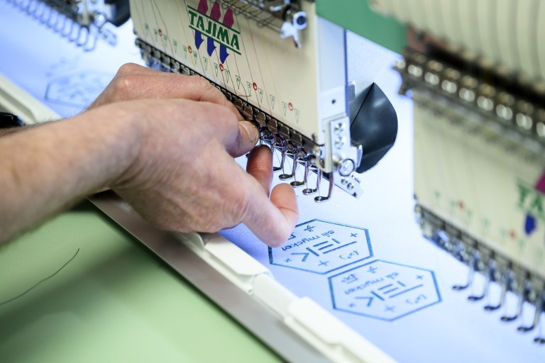 Lähikuvassa asetetaan lankaa brodeerauskoneen neulaan.