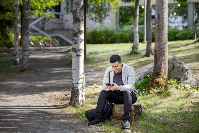 Nuori mies istuu kannolla puhelin kädessä