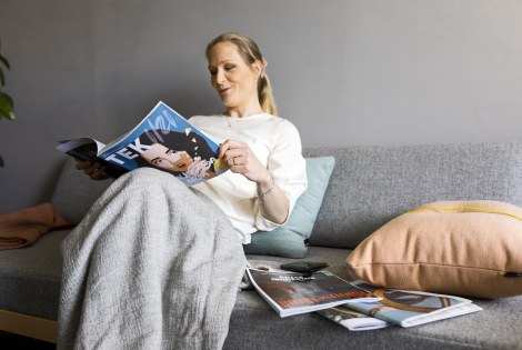 Henkilö rentoutumassa lehden kanssa sohvalla