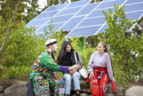 Opiskelijoita haalarit jalassa aurinkopaneelin edessä.