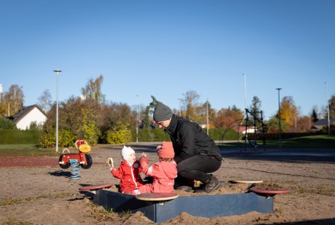 Nuori isä leikkii lastensa kanssa hiekkalaatikolla.