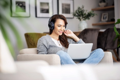 Aikuinen istuu kotonaan kannettavan tietokoneen ääressä kuulokkeet päässään.