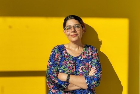 Negar Sharifi leaning on a sun-lit yeallow wall.