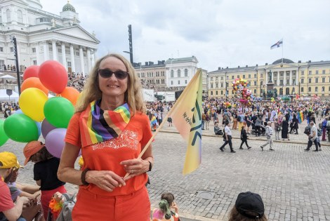 Sirkku Pohja seisoo Senaatintorin laidalla, kädessään TEKin sateenkaaren värinen lippu.