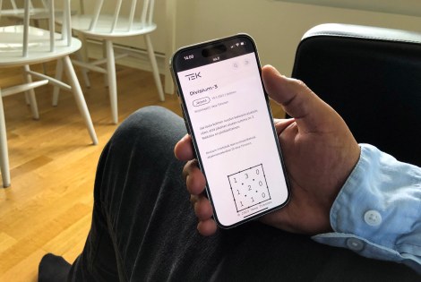 Kotioloissa istuva henkilö pitää kädessään kännykkää, jossa on auki Divisium-3-peli.