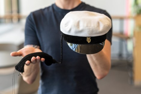 Henkilö pitää teekkarilakkia toisessa kädessään ja sen tupsua toisessa.