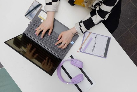 Ylhäältä päin otettu kuva henkilöstä, joka käyttää kannettavaa tietokonetta.