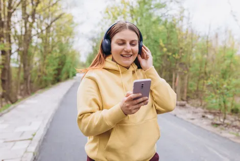 nainen, keltainen huppari, kännykkä, kuulokkeet