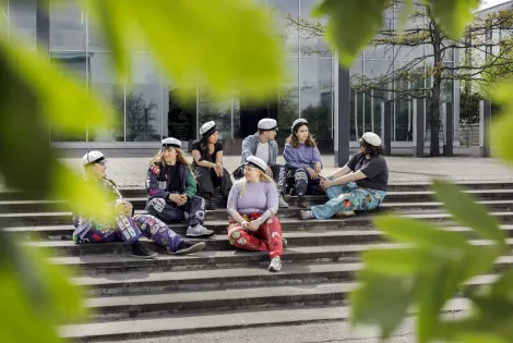 Opiskelijoita istumassa ulkona portaikossa, kesän vihreitä lehtiä etualalla.