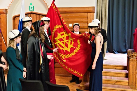 Juhla-asuisia ihmisiä teekkarilakit päässään lipun ympärillä.