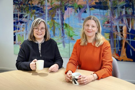 Satu Myller ja Maisa Holm istuvat pöydän ääressä, takana värikäs maalaus.