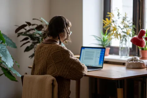 Nuorehko neisoletettu istuu tietokoneen ääressä kotonaan.