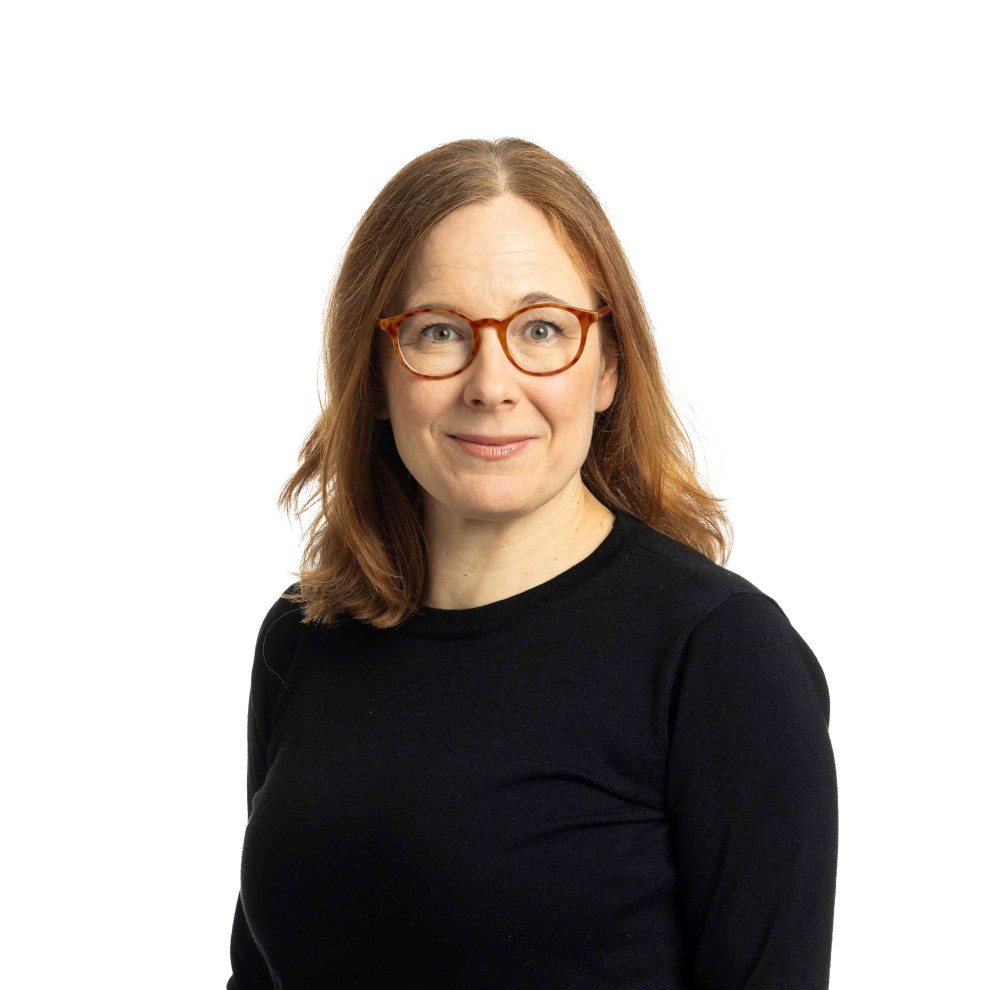 studiokuva ehdokaasta Tiina Davidsainen, hymyilevä nainen, jolla on punertavat hiukset, punertavat silmälasit ja musta pusero