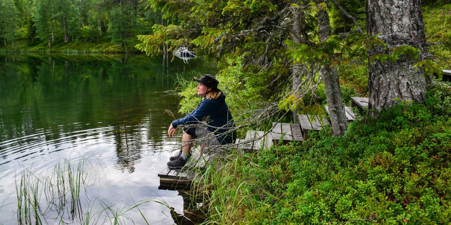 Henkilö istuu laiturilla järven rannalla. 