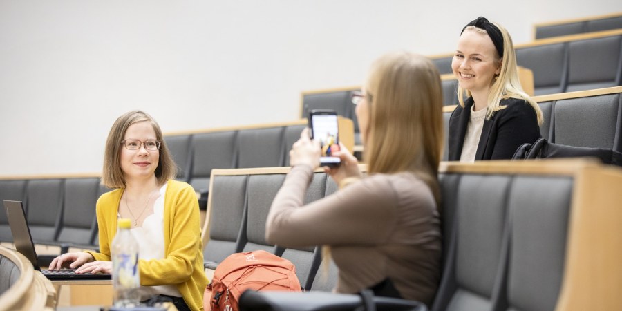 Opiskelijat luentosalissa, yksi kuvaa toista puhelimella.