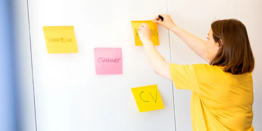 Uravalmentaja laittaa post-it lappuja valkotaululle